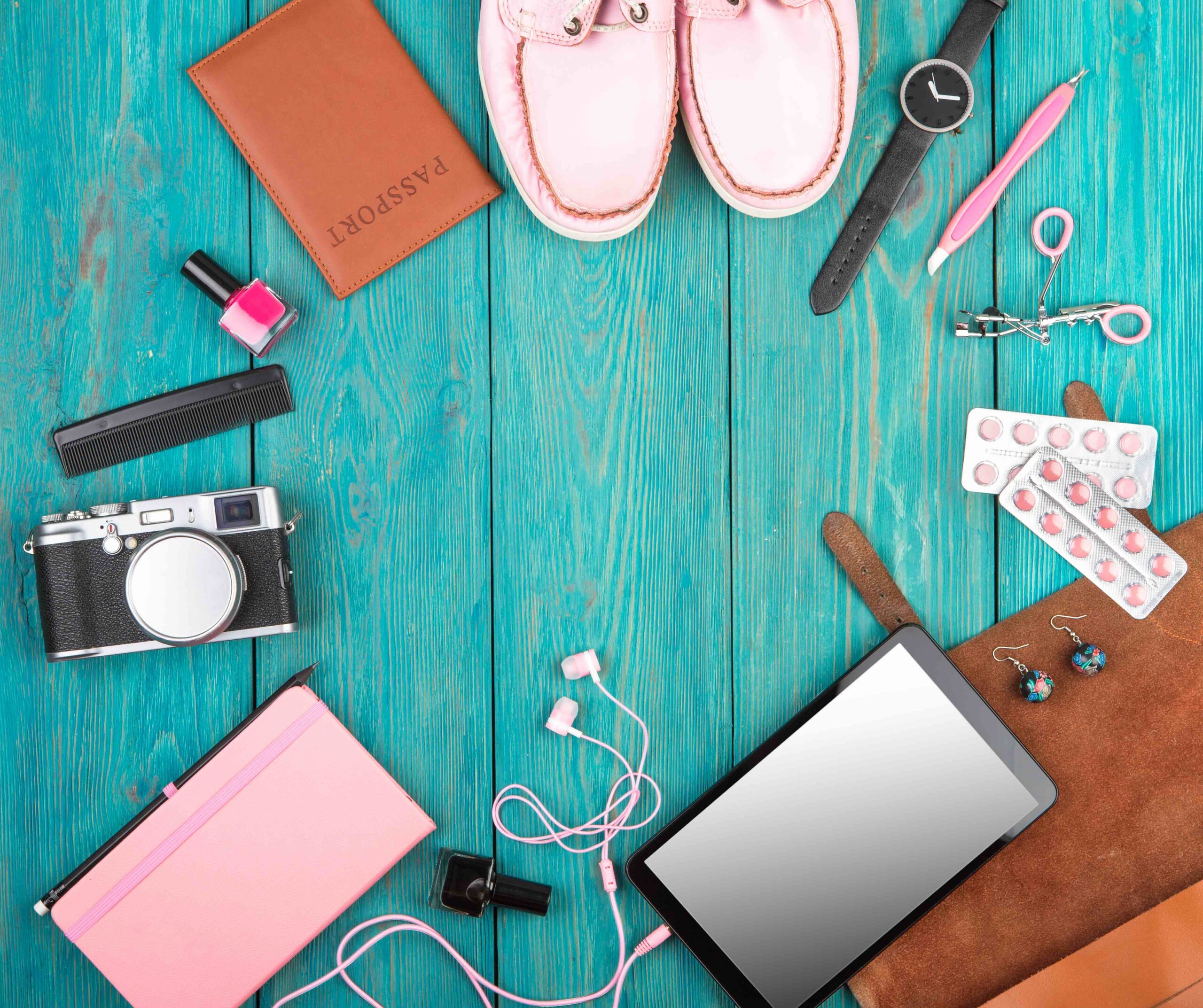 Travel Products- shoes, tablet pc, passport, camera, notepad, watch, headphones and essentials on blue wooden desk