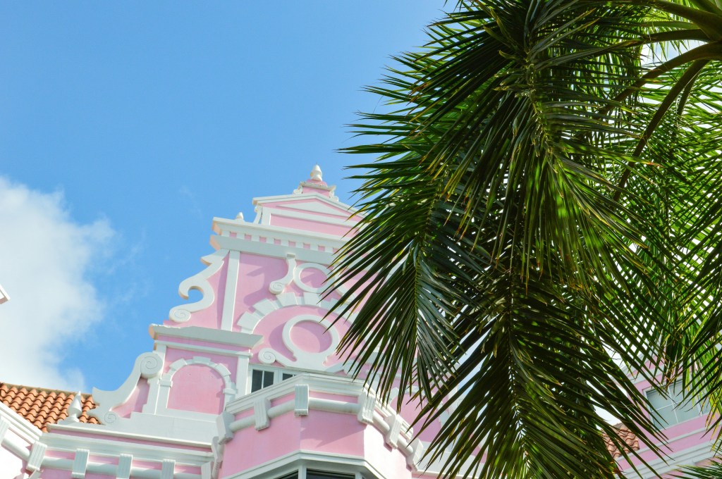 Pink and white building with a palm tree in front of it in Oranjestad, Aruba