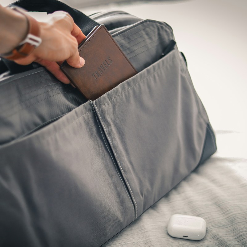 A person holding a passport in a bag on a bed